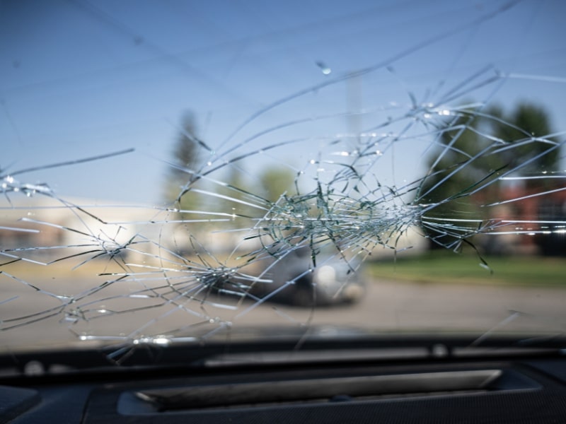 Severe car windscreen damage with multiple spider-web cracks viewed from inside the vehicle on a clear day.