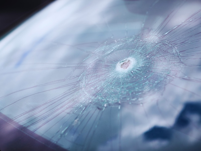A close-up view of a windshield with a prominent chip, showing cracks spreading outwards.