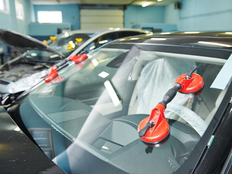 Red suction tools attached to car glass during fitting a windscreen process in workshop.