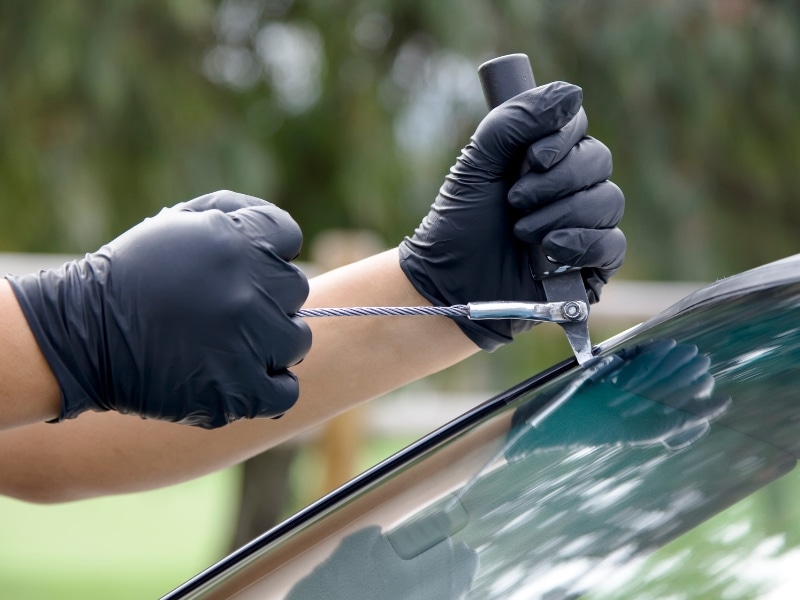 Technician using wire tool for mobile windscreen crack repair on car glass