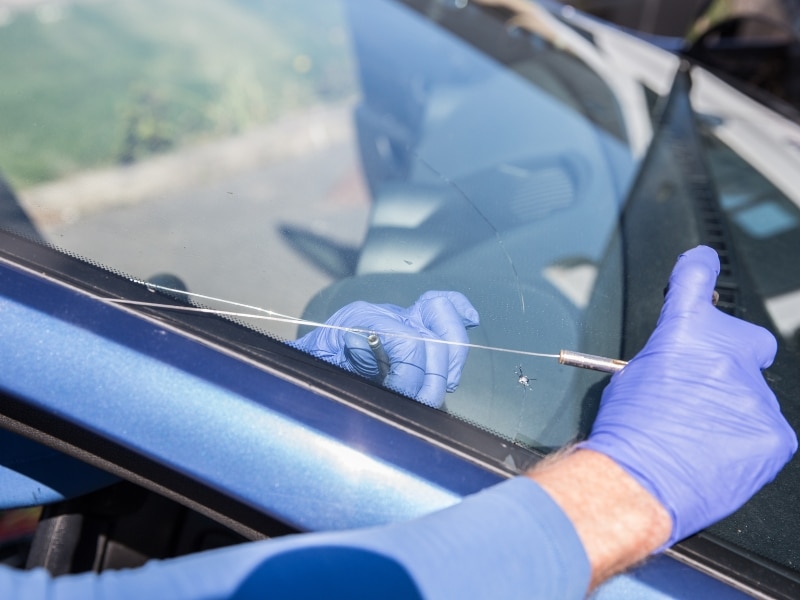 Technician repairing cracked windshield using a resin injector on a blue car
