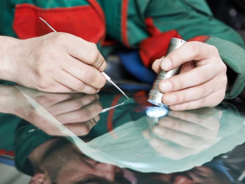 Specialist repairing cracked windshield under focused lighting in workshop