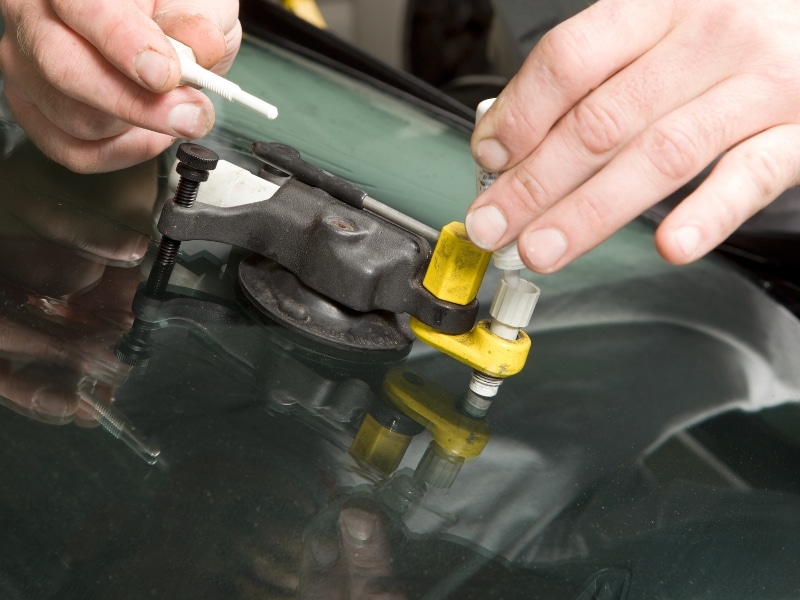 Technician injecting resin to repair stone chip in windscreen.