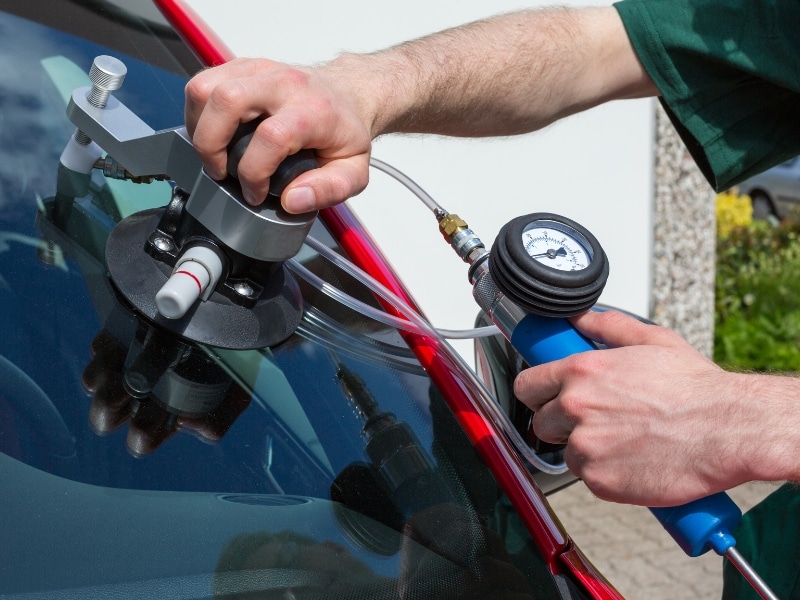 Technician using suction tool to repair stone chip in windscreen.